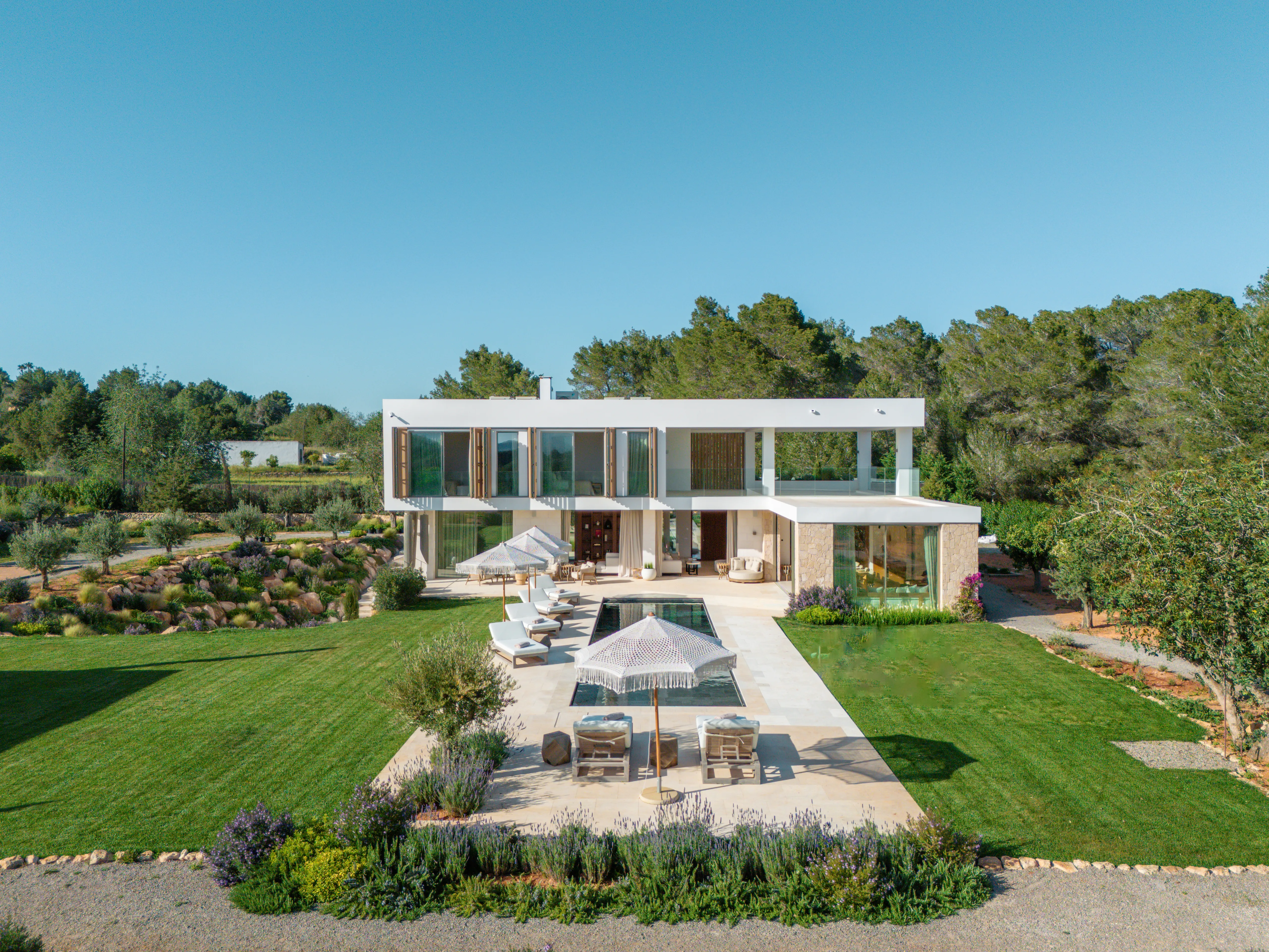 Villa blanca con jardín, piscina y sombrillas en el campo de Ibiza